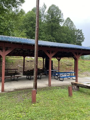 A covered picnic area with benches and picnic tables, surrounded by trees.