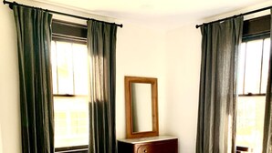 Une chambre à coucher avec un lit, une commode, une chaise et une fenêtre avec des rideaux.