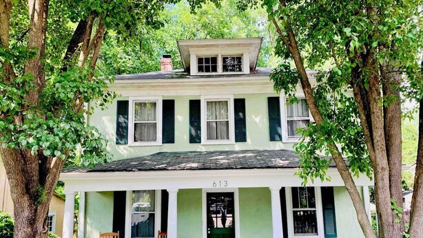 Une maison à deux étages avec un porche, portant le numéro 613, entourée d’arbres.