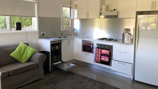 A compact kitchen with white cabinets, a stove, a microwave, and a refrigerator. - Animal friendly (Terrey Hills)