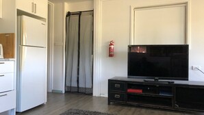 A modern living room with a flat-screen TV, a black entertainment unit, a white refrigerator, and a grey rug. - Animal friendly (Terrey Hills)