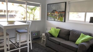 A room with a white desk, a grey sofa with green cushions, and a painting on the wall. - Animal friendly (Terrey Hills)