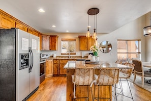 A modern kitchen with wooden cabinets, a stainless steel refrigerator, a central island with bar stools, and pendant lighting. - Beautiful Cabin W/ Gorgeous Lake Views, Private Hot Tub, Free WiFi & Large Deck (Garden City)