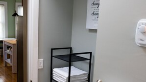Un bany amb una prestatgeria metàl·lica negra que conté tovalloles doblegades, una tovallola blanca penjada a un suport i un cartell al mur.