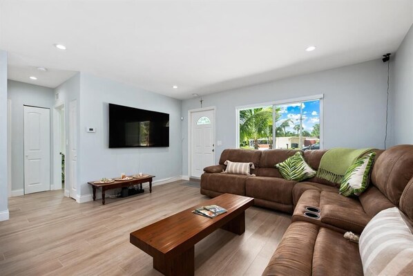 A modern living room with a brown leather sofa, a wooden coffee table, and a flat-screen TV mounted on the wall. - Beach House: Walk 2 Blocks to Beach & Pet Friendly (Hutchinson Island)