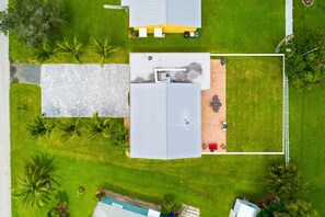 An aerial view of a residential property with two detached houses, a swimming pool, and a well-maintained lawn with palm trees.