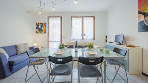 Een moderne woonkamer met een glazen eettafel, een blauwe bank en een schilderij aan de muur.