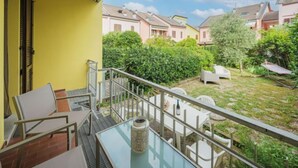 Een balkon met een glazen tafel, witte stoelen en een kleine bloempot.