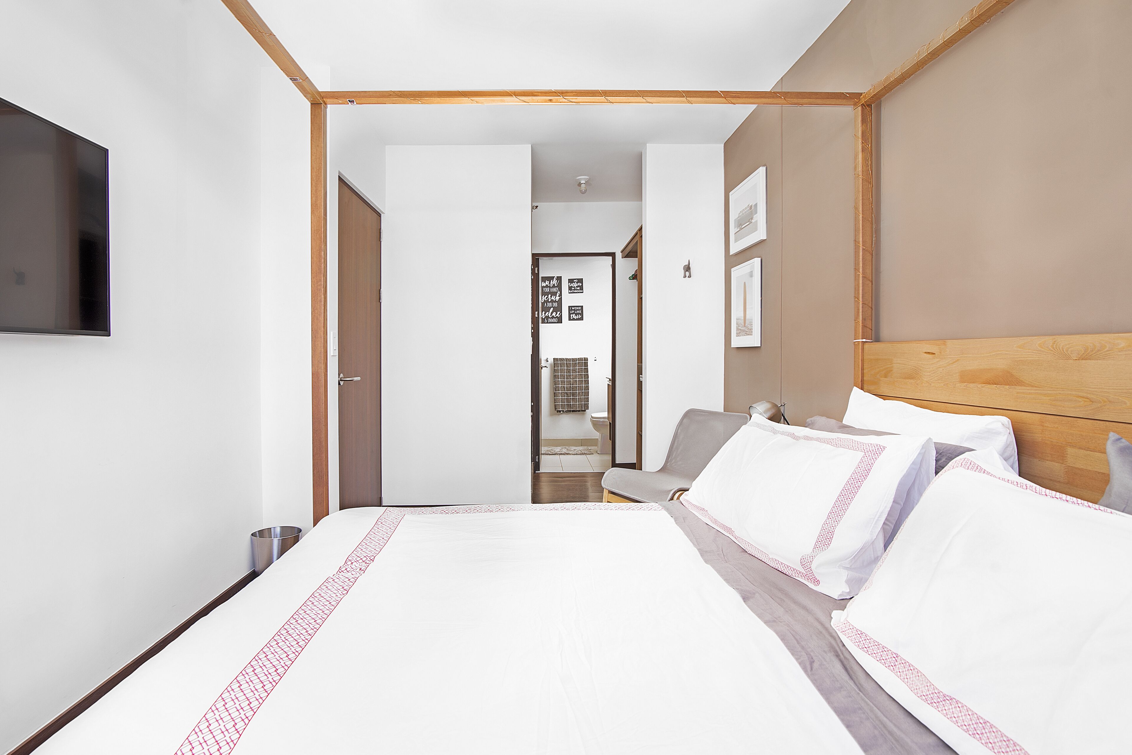 A hotel room with a bed, a TV mounted on the wall, and a wooden headboard.