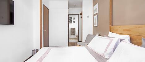 A hotel room with a bed, a TV mounted on the wall, and a wooden headboard.