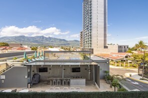 Un bar en la azotea con mesas al aire libre, un televisor y vistas a montañas y un edificio alto.