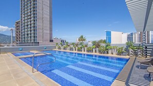 Piscina en la azotea con vistas a un edificio alto y palmeras.