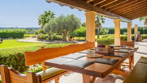 Un área de comedor al aire libre con bancos de madera y una mesa, rodeada de follaje y vistas al campo.
