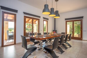Un vaste espace dédié à la salle à manger, avec une grande table en bois, des chaises noires et des luminaires suspendus.