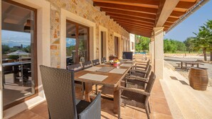 Un espacio para comer al aire libre con pared de piedra, pérgola de madera y sillas de mimbre.
