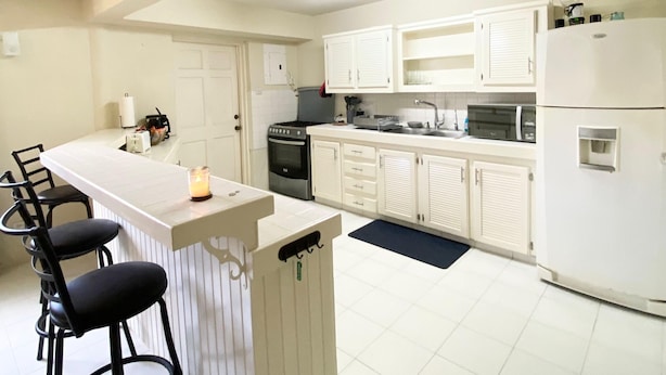 Una cocina moderna con armarios blancos, una isla central con taburetes y electrodomésticos como refrigerador y estufa.