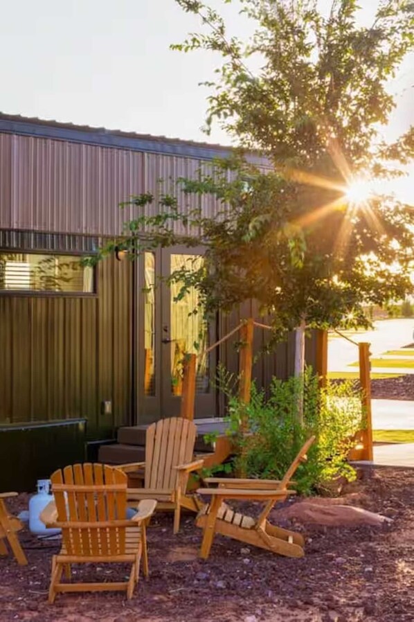 A building with a corrugated metal exterior, a wooden deck with Adirondack chairs, and a tree in the foreground.