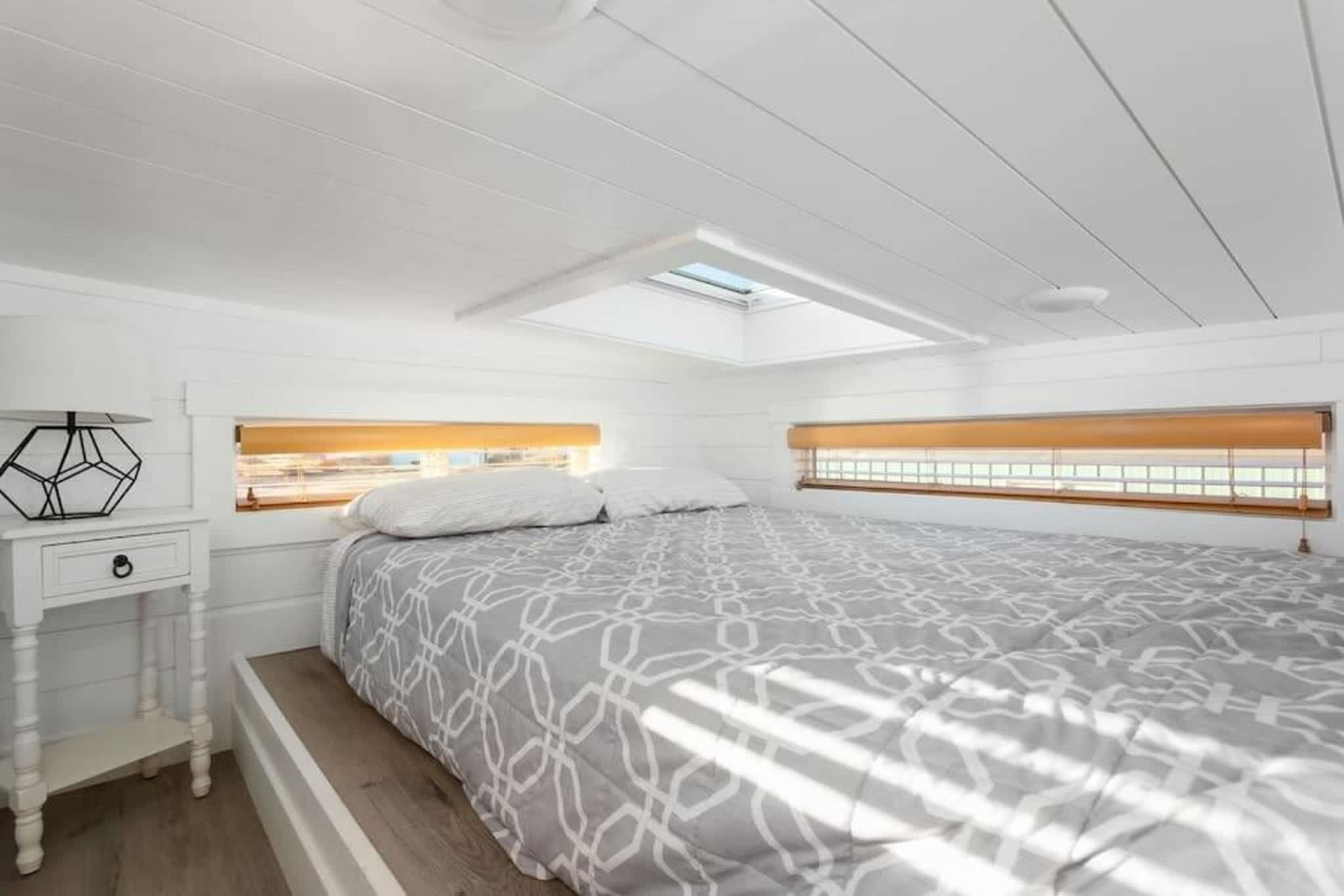 Een slaapkamer met dakraam, een bed met decoratieve beddengoed, een nachtkastje en een kledingkast.