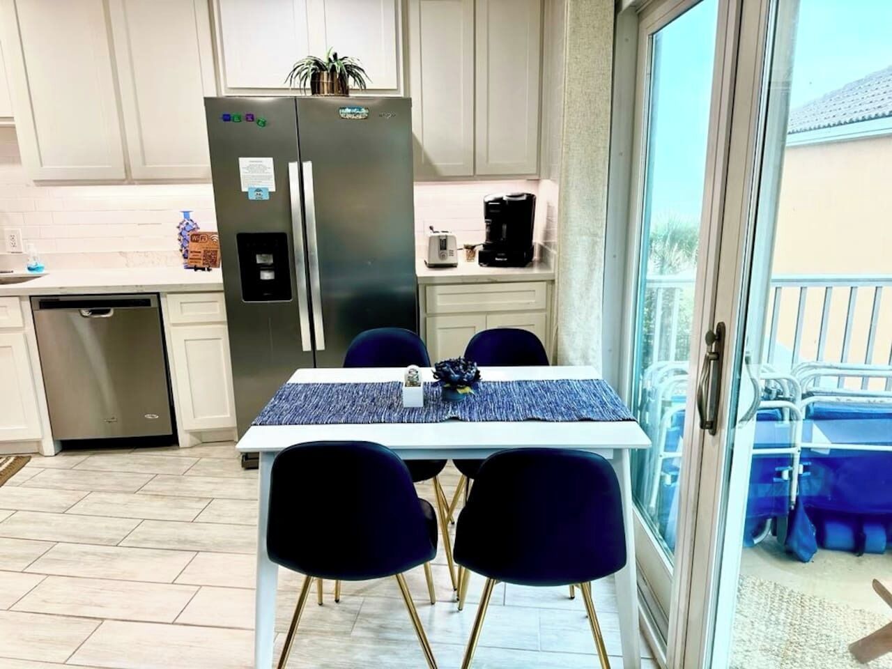 A kitchen with a refrigerator, coffee maker, and dining table with chairs.