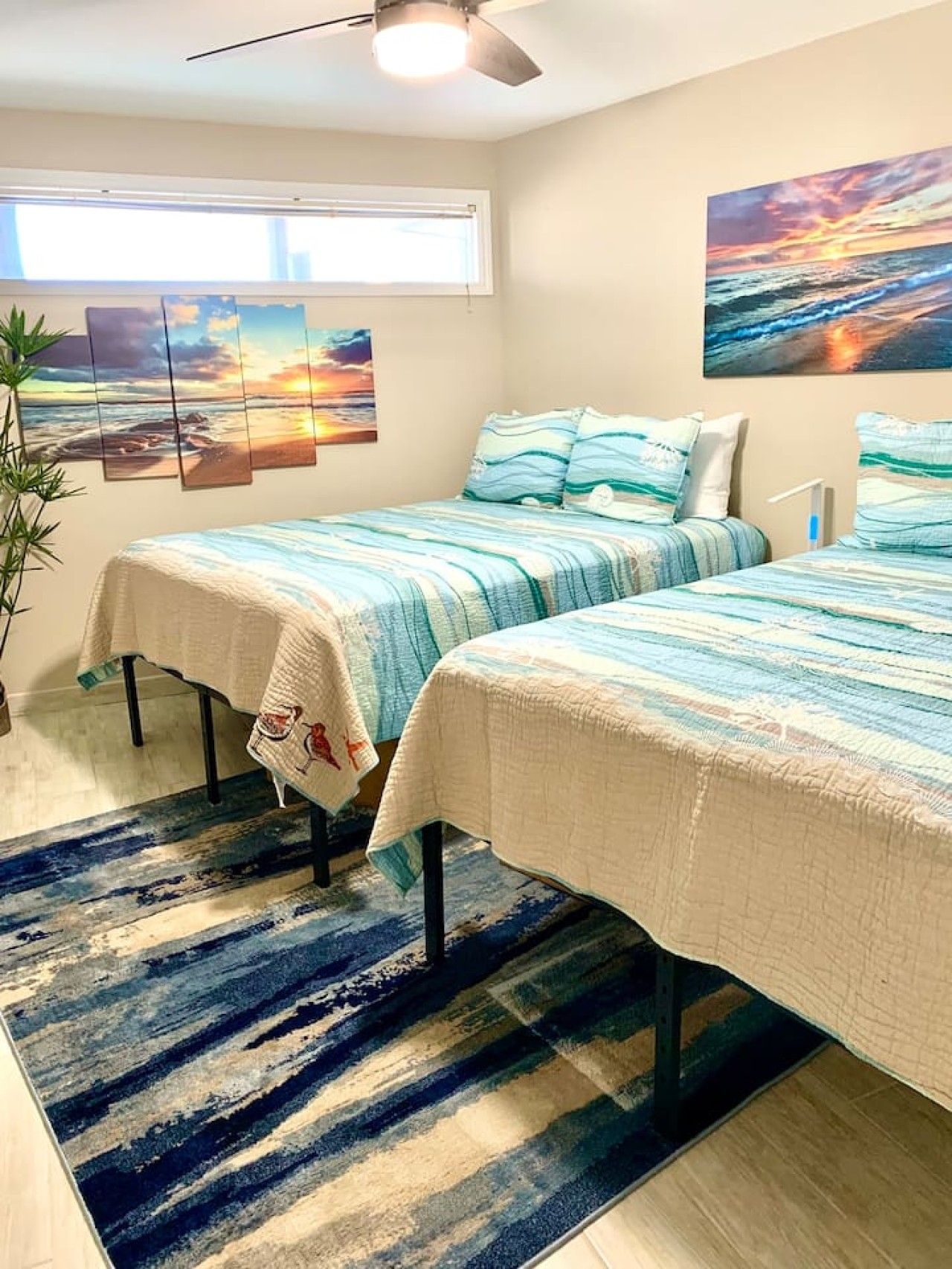 Un dormitorio con dos camas, un ventanal grande y un cuadro de una puesta de sol.