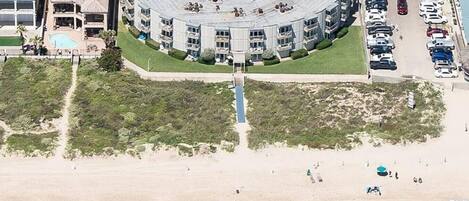 A beachfront hotel with a central courtyard, a swimming pool, and a parking lot.