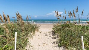 Een zandpad langs het strand dat naar de oceaan leidt, met hoge grassen aan beide kanten.