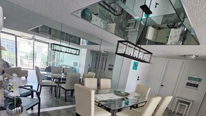 A modern dining area with a glass table and chairs, a high ceiling with a skylight, and a view of the outdoors. - Large Fort Myers Beach 2 Bedroom Condo (Fort Myers Beach)