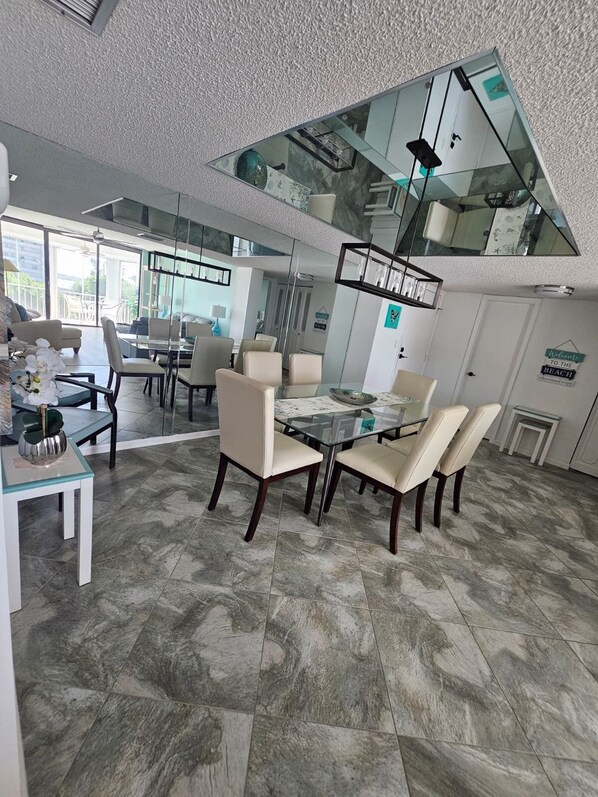 Un espace repas moderne avec une table et des chaises en verre, un plafond haut doté d’une verrière et une vue sur l’extérieur.