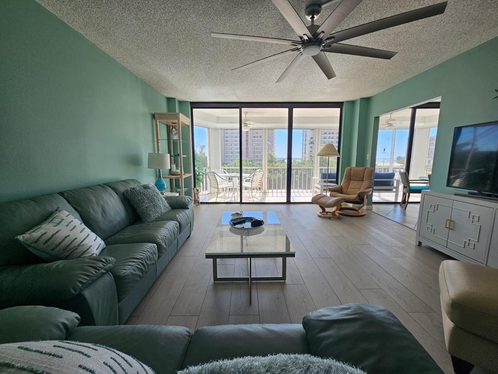 Un salon comprenant un canapé, une table basse, un téléviseur et un balcon aménagé avec du mobilier d’extérieur.