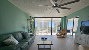 A living room with a sofa, a coffee table, a TV, and a balcony with outdoor furniture. - Large Fort Myers Beach 2 Bedroom Condo (Fort Myers Beach)