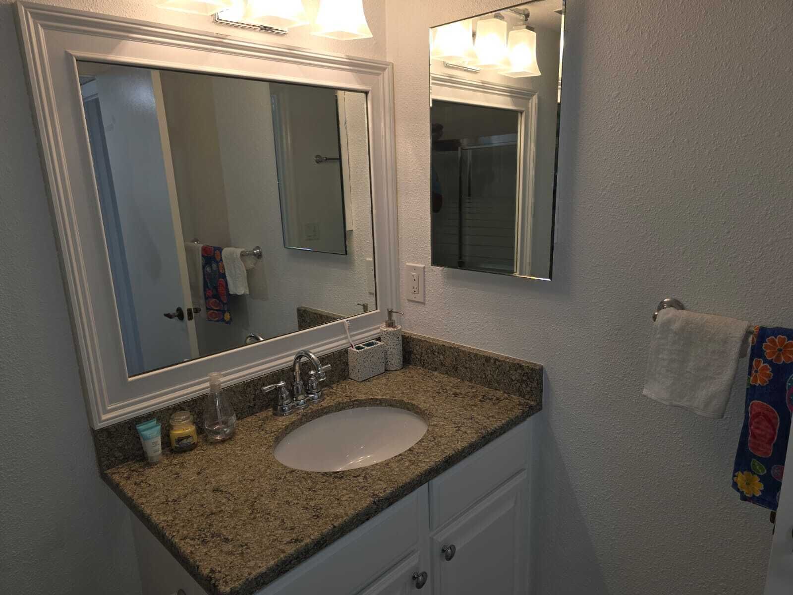 A bathroom with a granite countertop sink, a large mirror, and a towel rack with a floral towel.