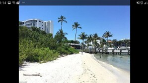A beach with white sand, palm trees, and a building in the background. - Large Fort Myers Beach 2 Bedroom Condo (Fort Myers Beach)