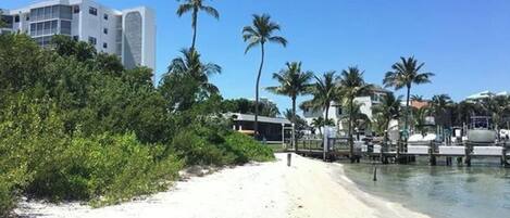 Una playa de arena blanca, palmeras y un edificio al fondo.