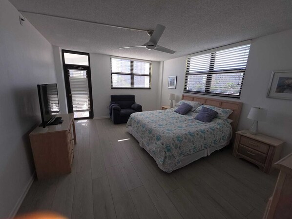 A bedroom with a bed, a chair, a TV, and a ceiling fan.