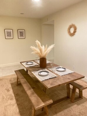 Un comedor con una mesa de madera preparada para cuatro personas, bancos y un jarrón con plumas de plumas.