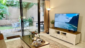 Un salon avec un téléviseur, une table basse avec des magazines et une vue sur l’extérieur.