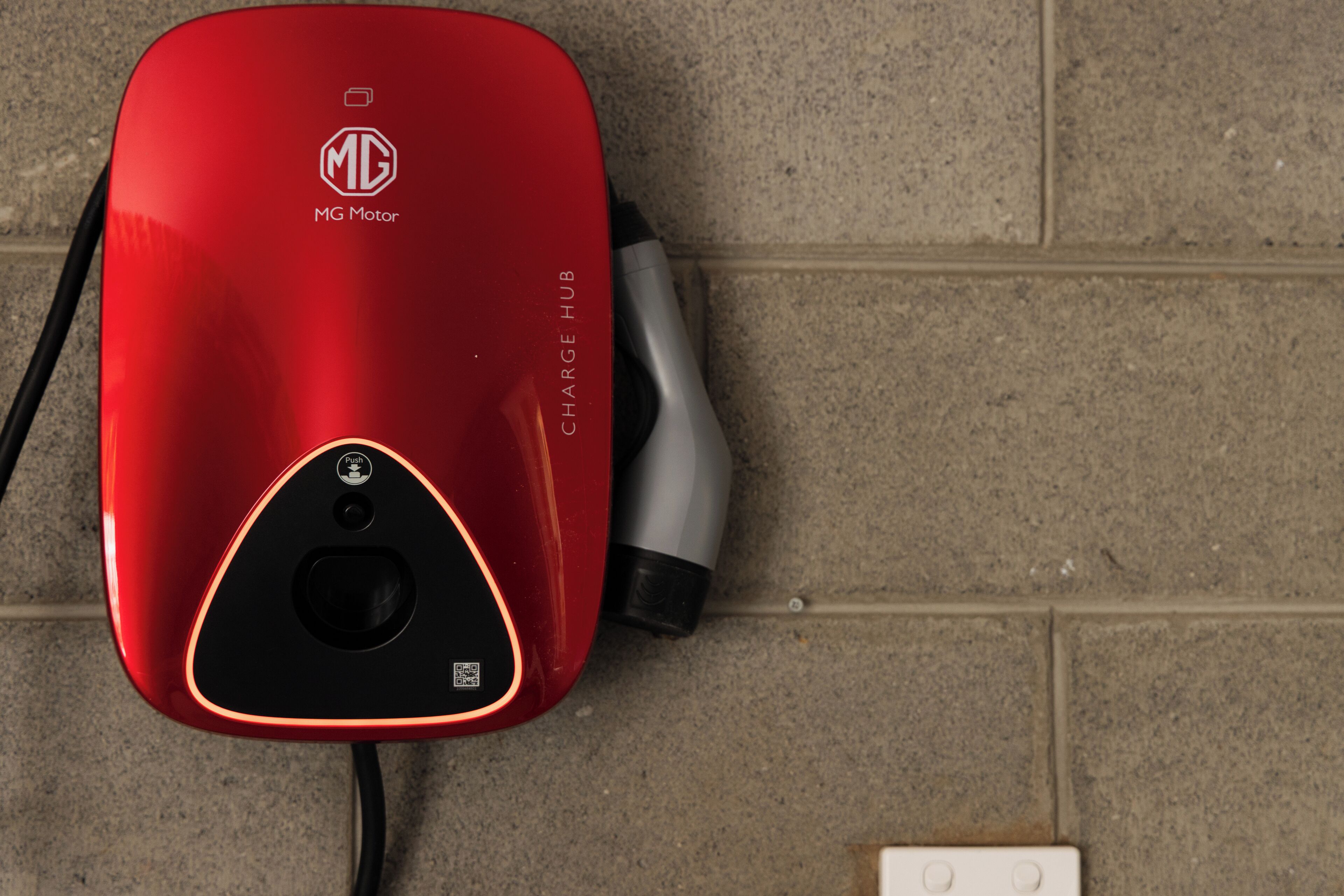 A red MG Motor electric vehicle charging station with a cable connected to it.