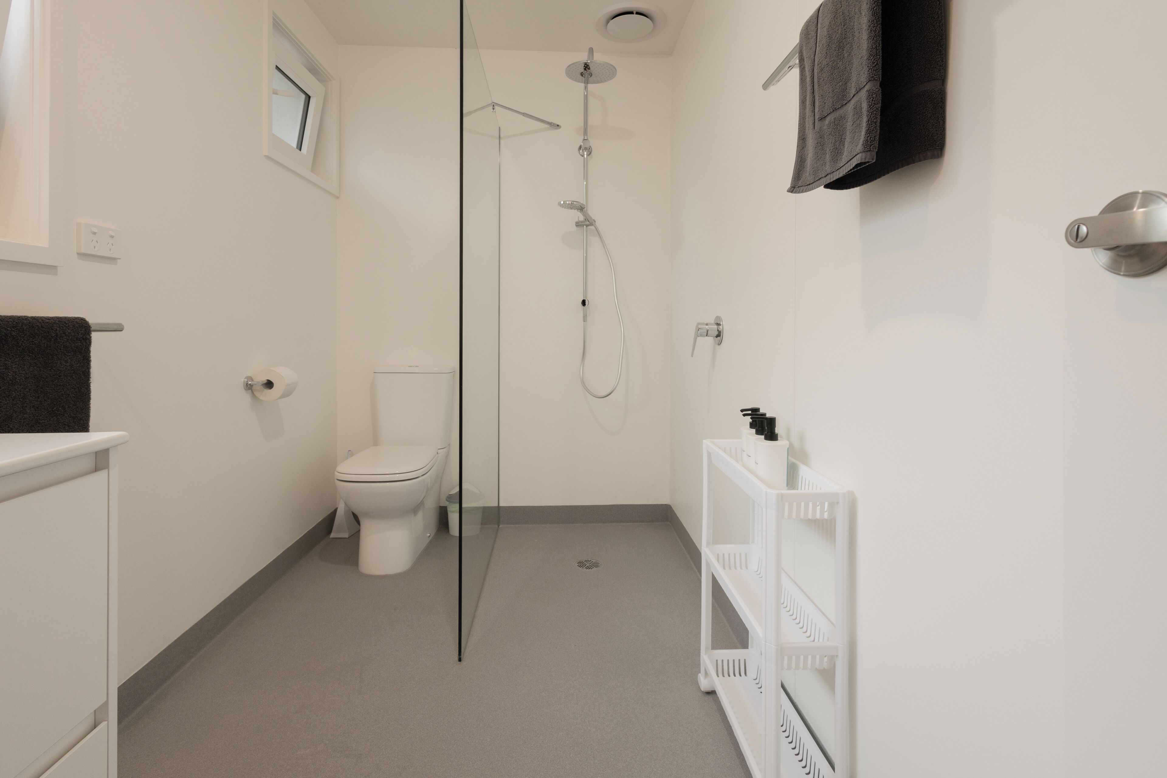 Une salle de bain moderne avec une douche à parois de verre, des toilettes et un meuble-lavabo blanc doté d’un porte-serviettes.