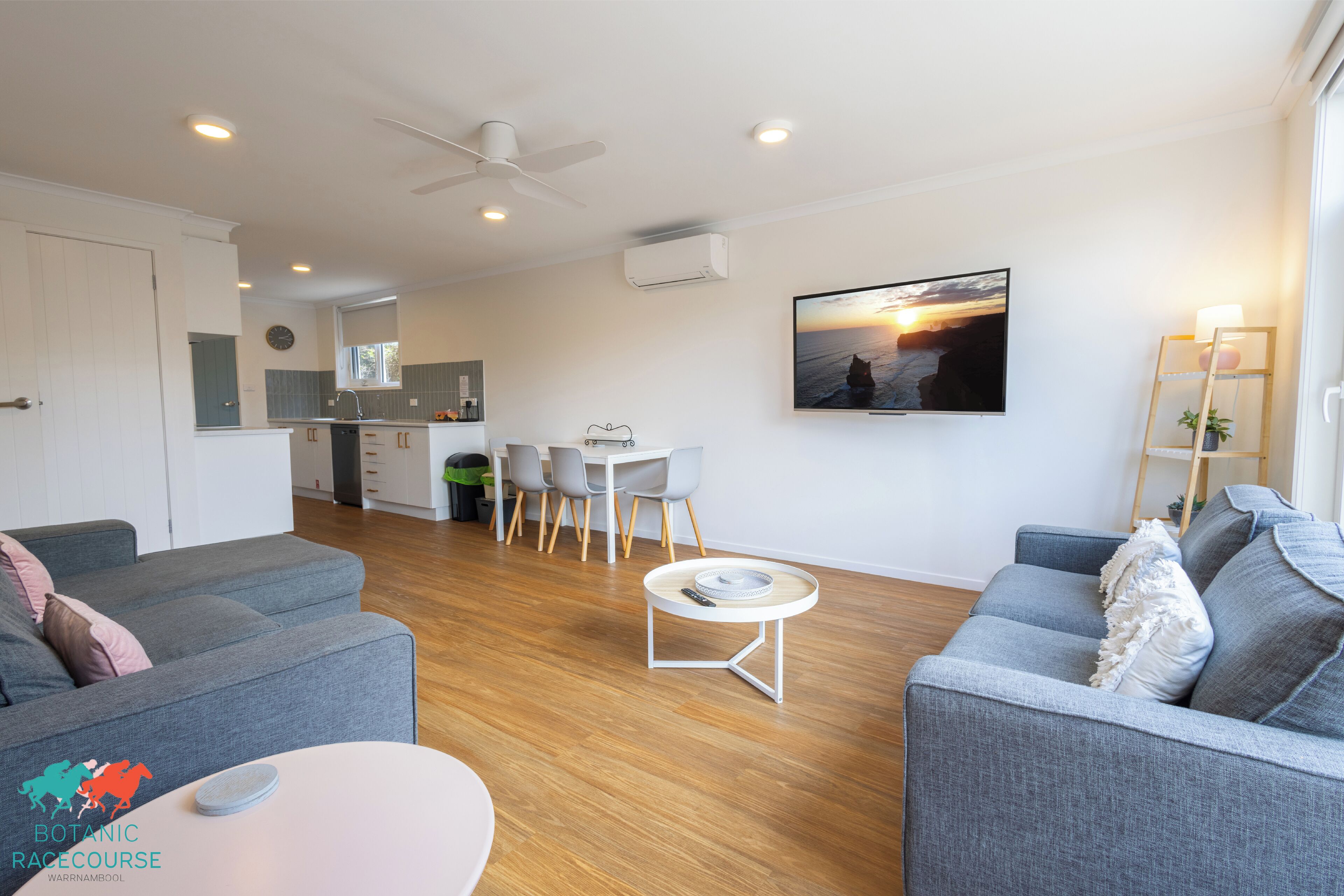 A modern living room with grey sofas, a coffee table, and a dining area with a white table and chairs.