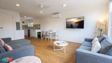 A modern living room with grey sofas, a coffee table, and a dining area with a white table and chairs.