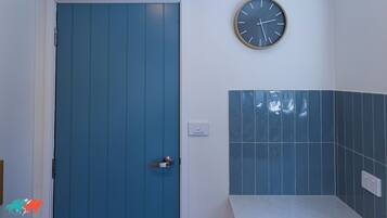 Un baño con puerta azul, un reloj en la pared y un salpicadero de azulejos.