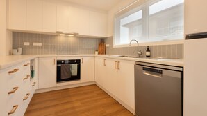 Cocina moderna con armarios blancos, horno empotrado, lavavajillas y ventana que proporciona luz natural.