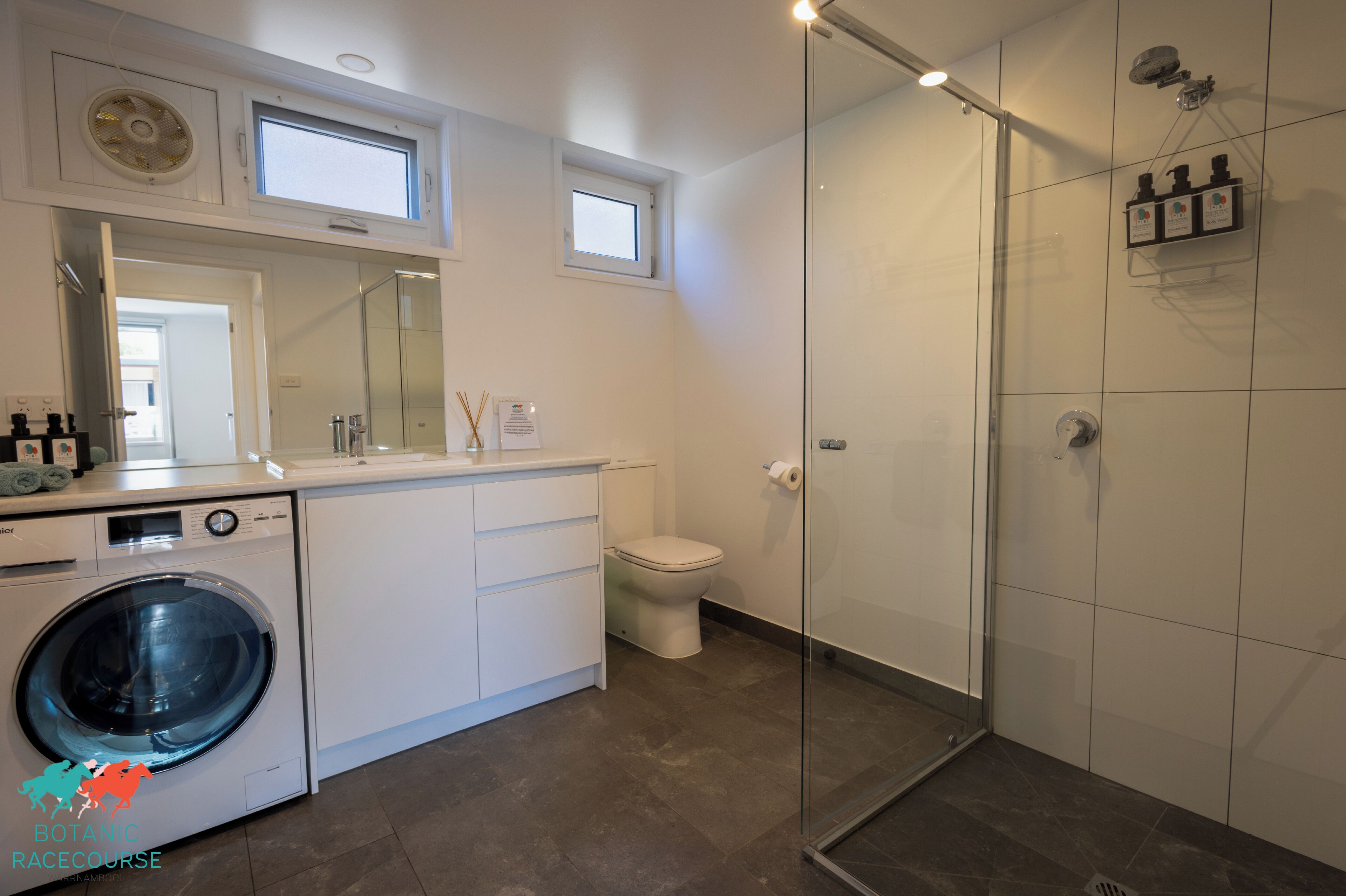 A modern bathroom with a glass-enclosed shower, a built-in washing machine, and a toilet.