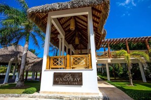 A beach club with a thatched roof structure, palm trees, and a sign indicating the name.