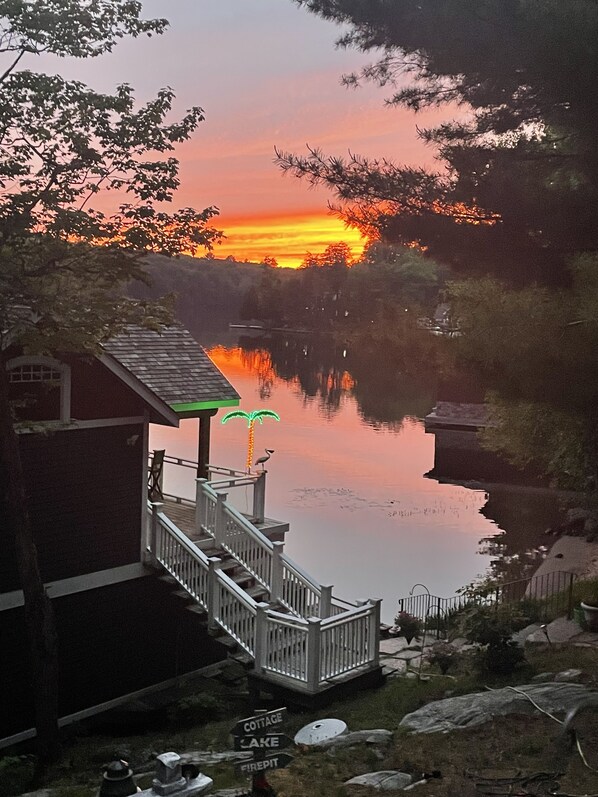 A dock with a railing, a small building with a porch, and a sign indicating directions to Cottage Lake and Firepit.