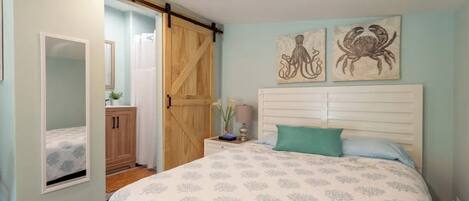 A bedroom with a bed, a nightstand, a mirror, a wardrobe, and two wall art pieces of a crab.