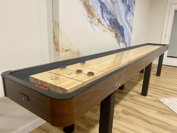 Una mesa de shuffleboard con zonas de puntuación numeradas, un logotipo y una pintura de mármol al fondo.