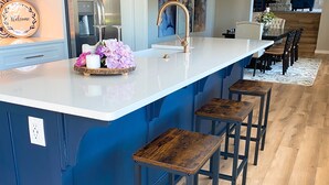 A modern kitchen with a central island, bar stools, and a dining area with a fireplace. - NEW! Luxury cottage with epic lake view (Rogers)