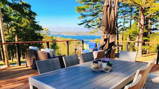 A deck with wicker furniture, a table, and a view of a lake. - NEW! Luxury cottage with epic lake view (Rogers)