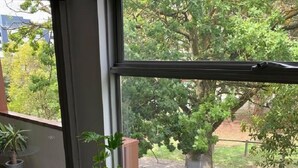 Ein Balkon mit Glastisch und Stühlen, Blumentöpfen und Blick auf Bäume und Gebäude.